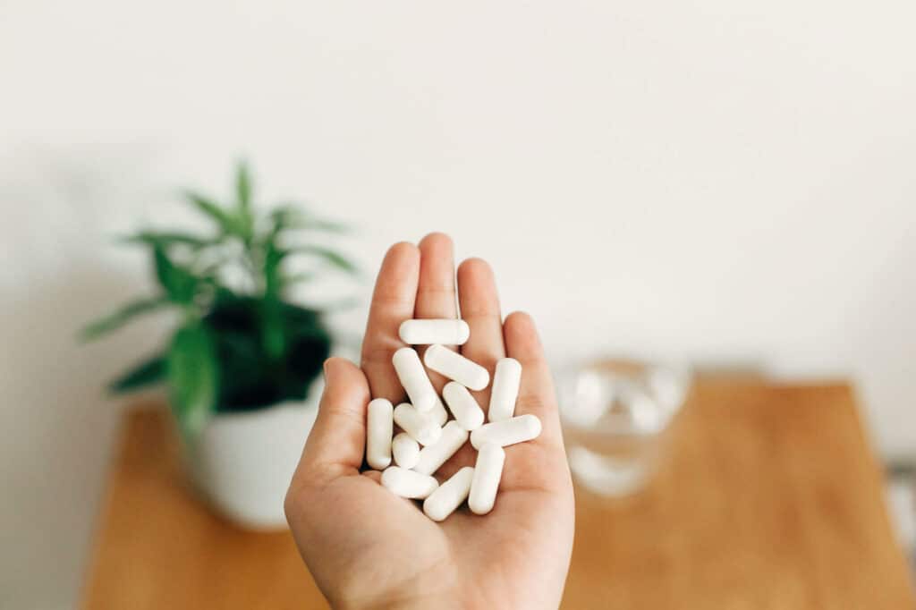 Person's hand holds out multiple white magnesium supplement capsules, How Much Magnesium Do You Need Daily