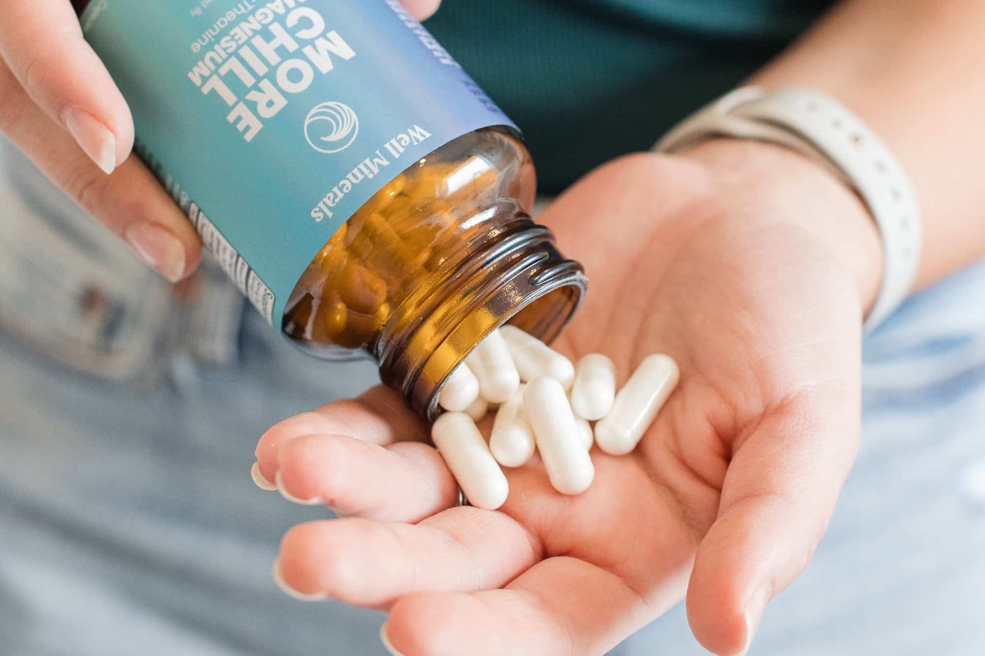 A bottle of magnesium lysinate glycinate opened and capsules pouring into the palm of a woman's hand.