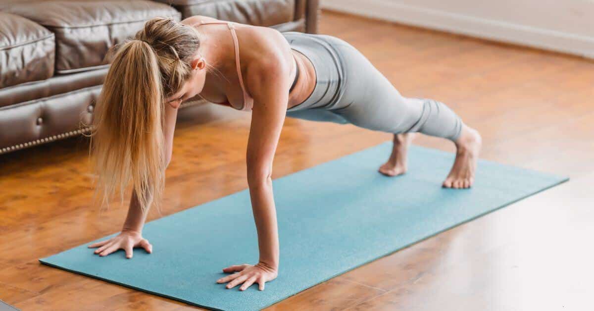 A fit woman holds a plank on a yoga mat in her living room