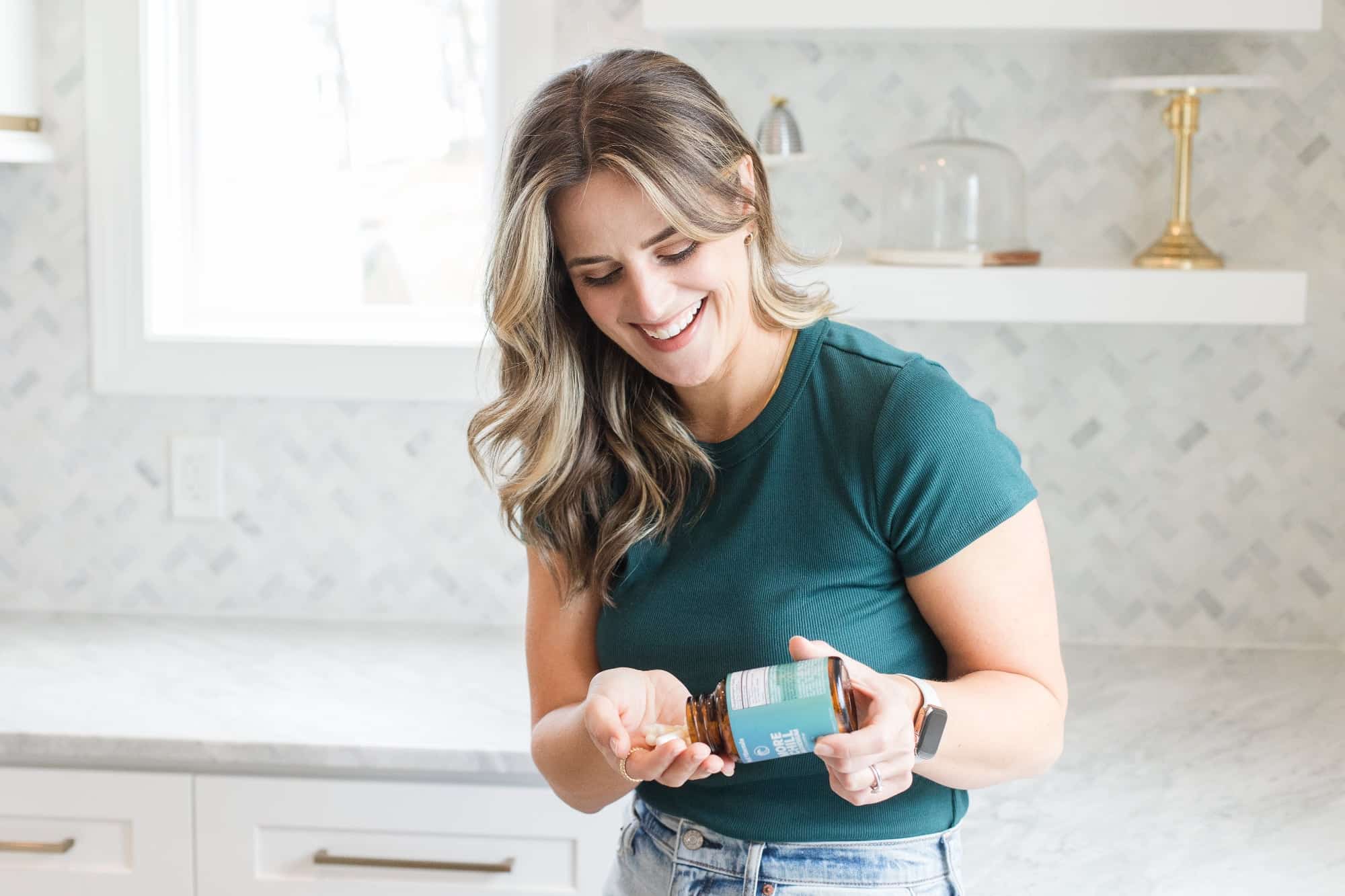 Noelle Tarr standing in the kitchen holding a bottle of magnesium lysinate glycinate and taking it.