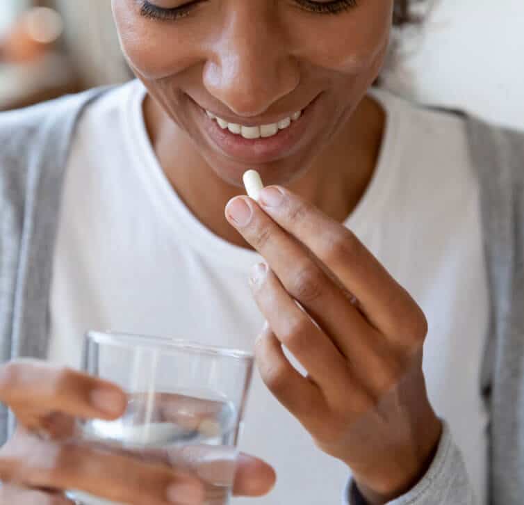 Smiling woman puts a white capsule of magnesium lysinate glycinate up to her lips