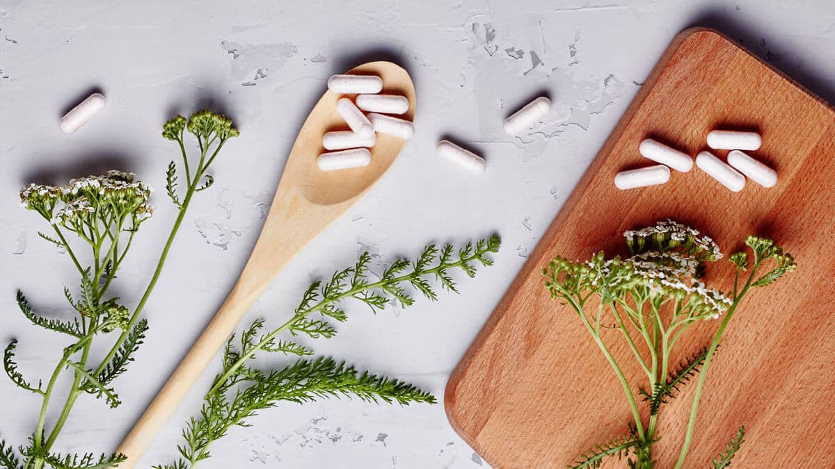 White pill capsules scattered with plants and a wooden spoon and cutting board, Magnesium Lysinate Glycinate Benefits