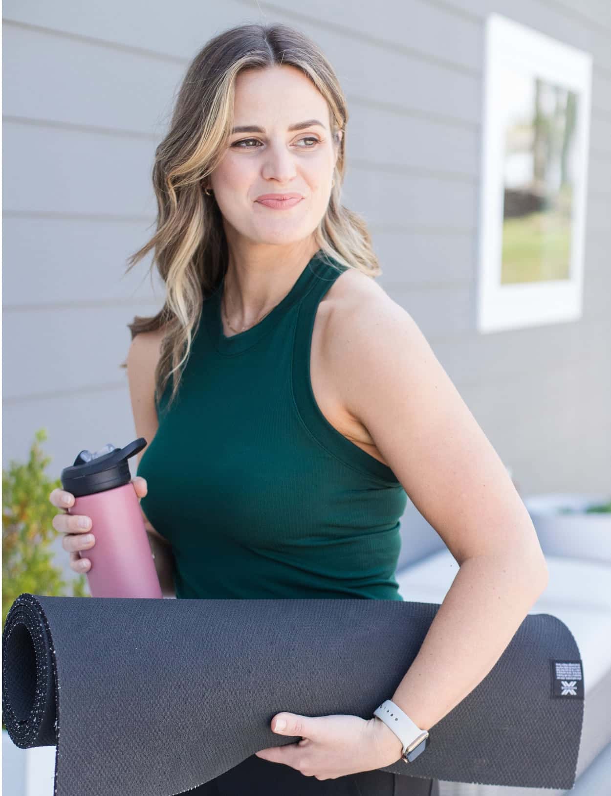 Noelle looks into the distance as she holds a yoga mat and water bottle, adrenal stress less