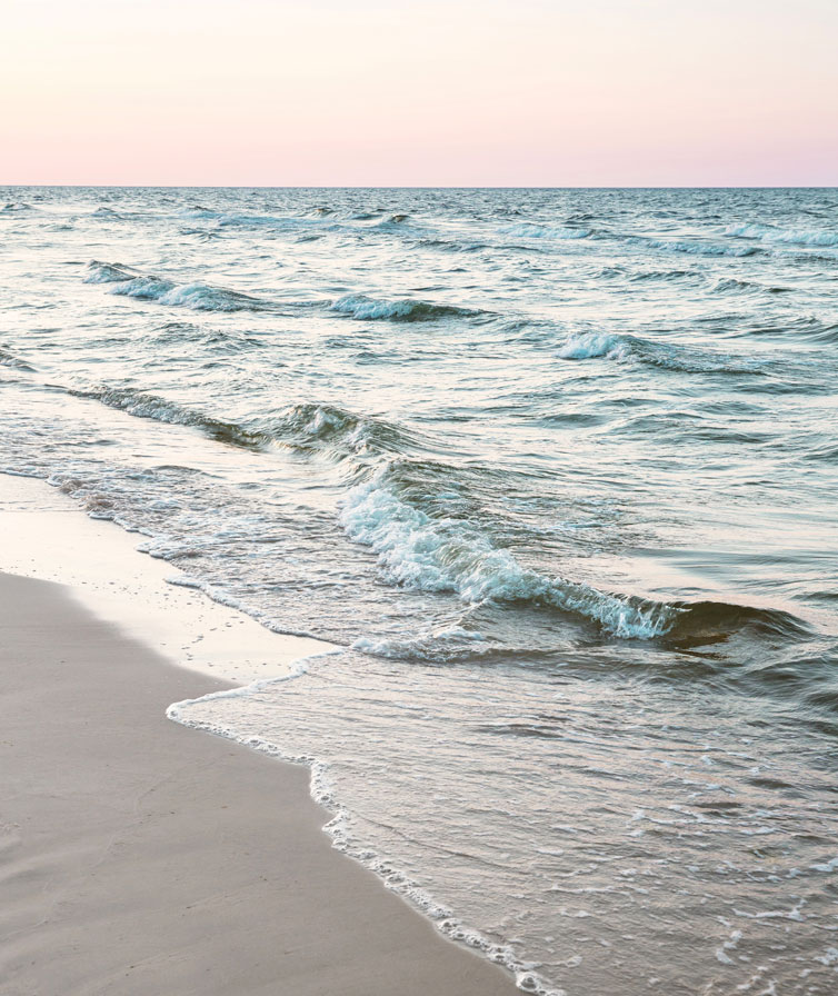 Waves roll onto a sandy beach shore in front of a relaxing and beautiful sunset